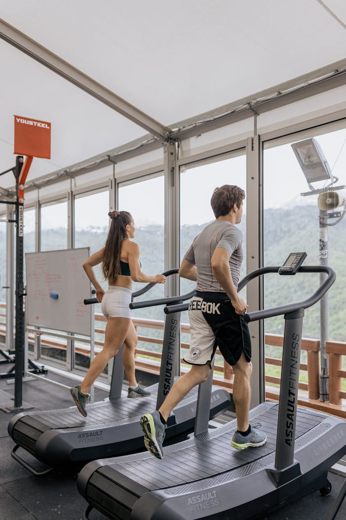 stats-img Man and woman running on treadmills in a bright gym with scenic views.